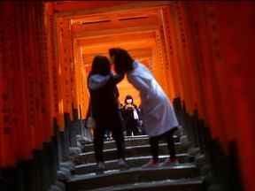 Les visiteurs portant des masques explorent les portes torii en bois du sanctuaire shinto Fushimi Inari Taisha à Kyoto, au Japon, le 13 mars 2020.