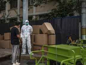 Un agent de santé porte une combinaison de protection alors qu'il se tient à côté de boîtes de déchets à enlever tout en parlant avec un passant à côté du mur de séparation d'un appartement sous verrouillage, après une récente épidémie de COVID-19 le 11 juin 2022 à Pékin.