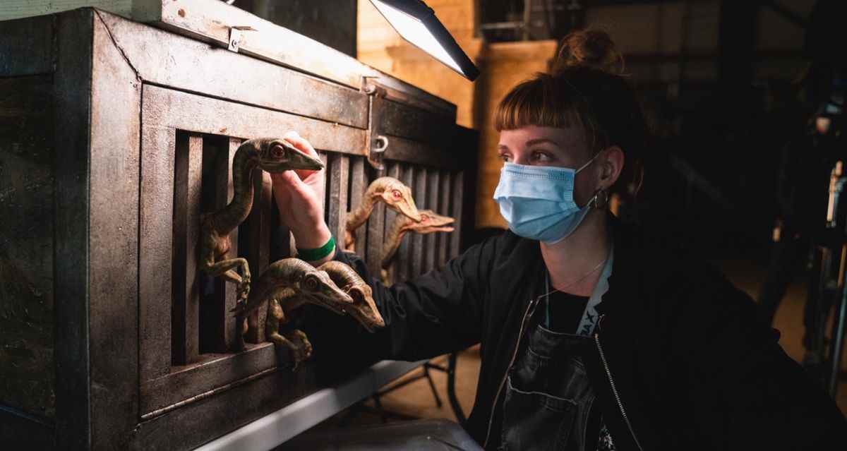 Une femme portant un masque chirurgical s'occupe d'une cage pleine de minuscules dinos dans Jurassic World: Dominion