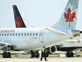 L'équipe au sol de la compagnie aérienne passe devant des avions d'Air Canada au sol alors qu'ils sont assis sur le tarmac de l'aéroport international Pearson, à Toronto, le mardi 27 avril 2021.
