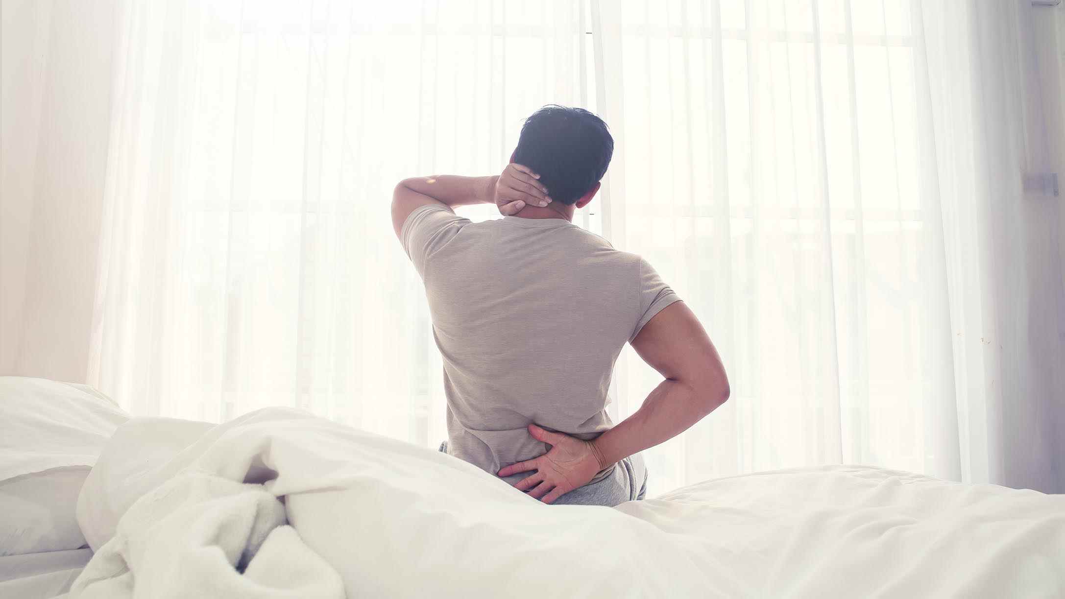Un homme s'assied dans son lit en tenant son dos douloureux