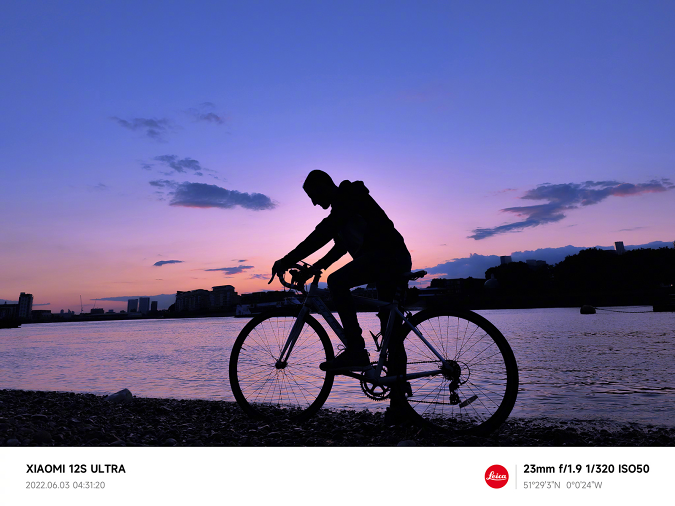 Un exemple de prise de vue prise avec le Xiaomi 12S Ultra, mettant en scène un cycliste au bord d'une rivière tôt le matin avant le lever du soleil.
