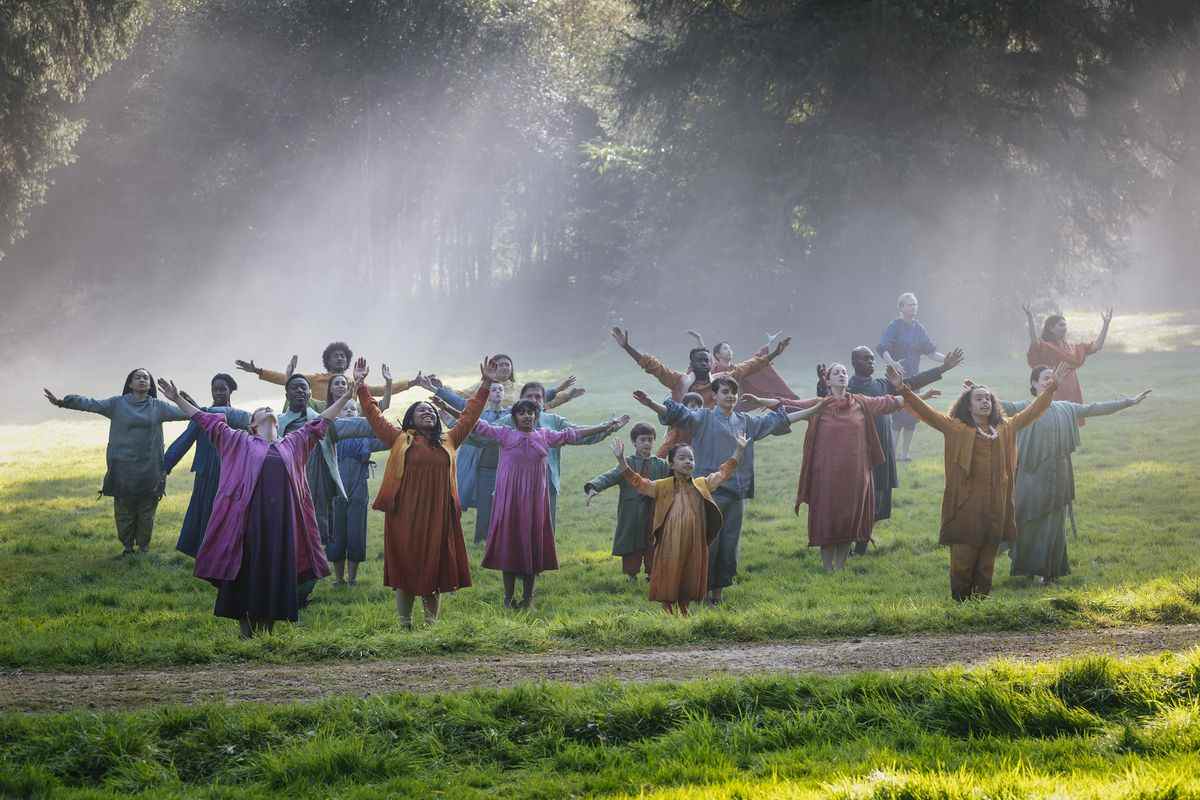 Un groupe de personnes vêtues de vêtements colorés levant les bras et s'ouvrant dans une clairière brumeuse