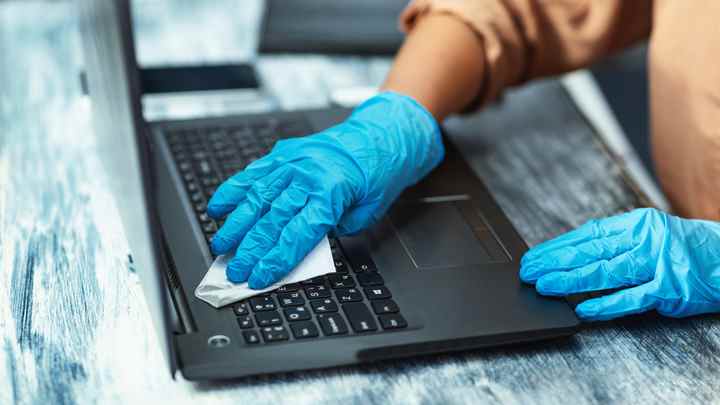 Comment nettoyer l'écran d'un ordinateur portable : une personne avec des gants bleus nettoie un ordinateur portable en surface