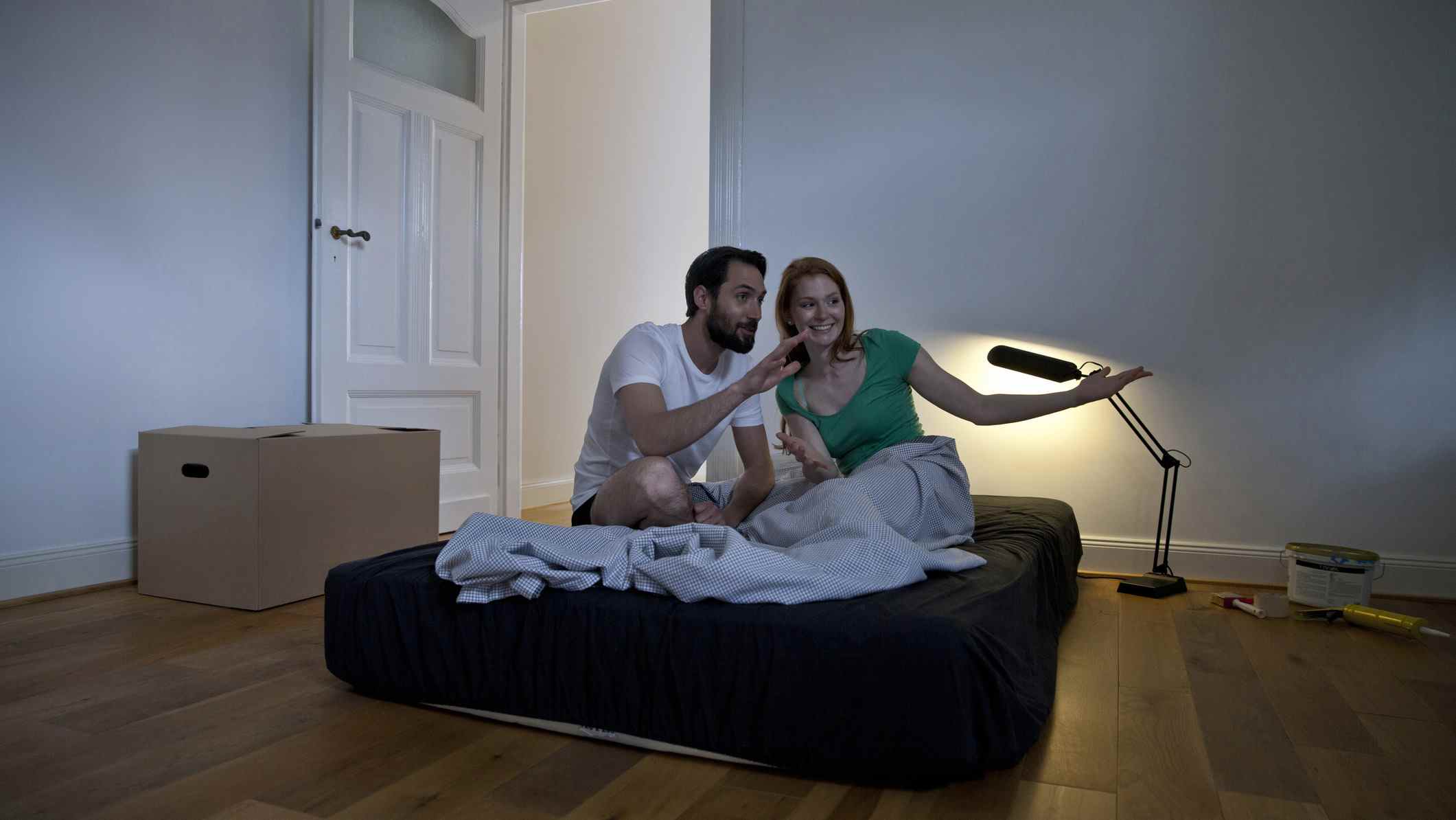 Un couple est assis sur un matelas recouvert de draps noirs dans une nouvelle chambre dans laquelle ils viennent d'emménager