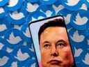 Une image d'Elon Musk est visible sur un smartphone placé sur des logos Twitter imprimés.