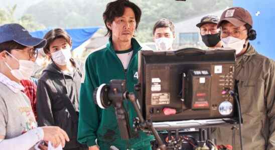 A man in a dark green tracksuit examines a television monitor, surrounded by others in masks; actor Lee Jung-jae behind the scenes of "Squid Game."