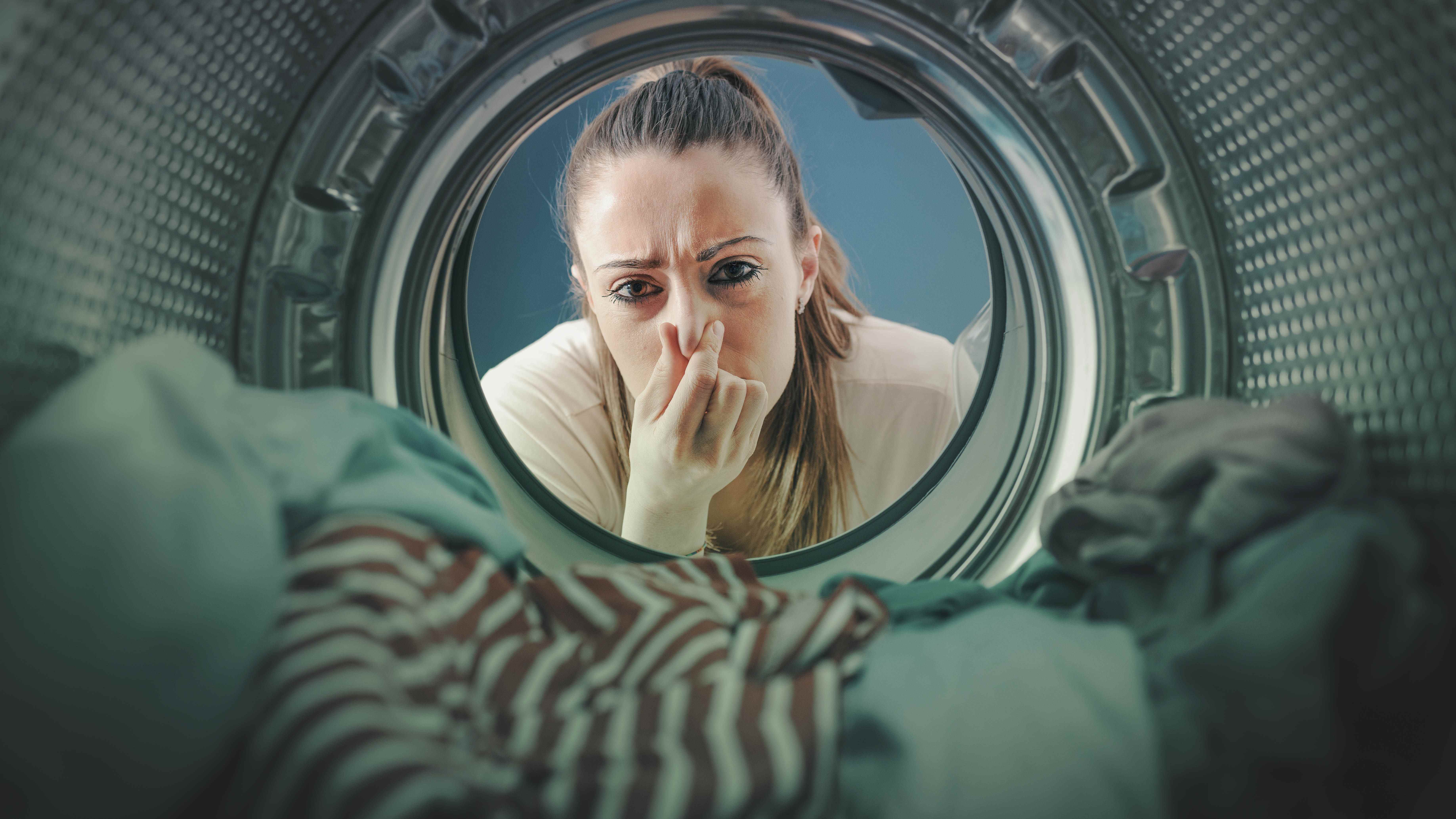 Une femme se tenant le nez alors qu'elle regarde le linge à l'intérieur de la machine à laver