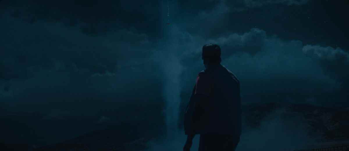 OJ (Daniel Kaluuya), vu en silhouette de dos la nuit, regardant un OVNI dans le ciel de Nope