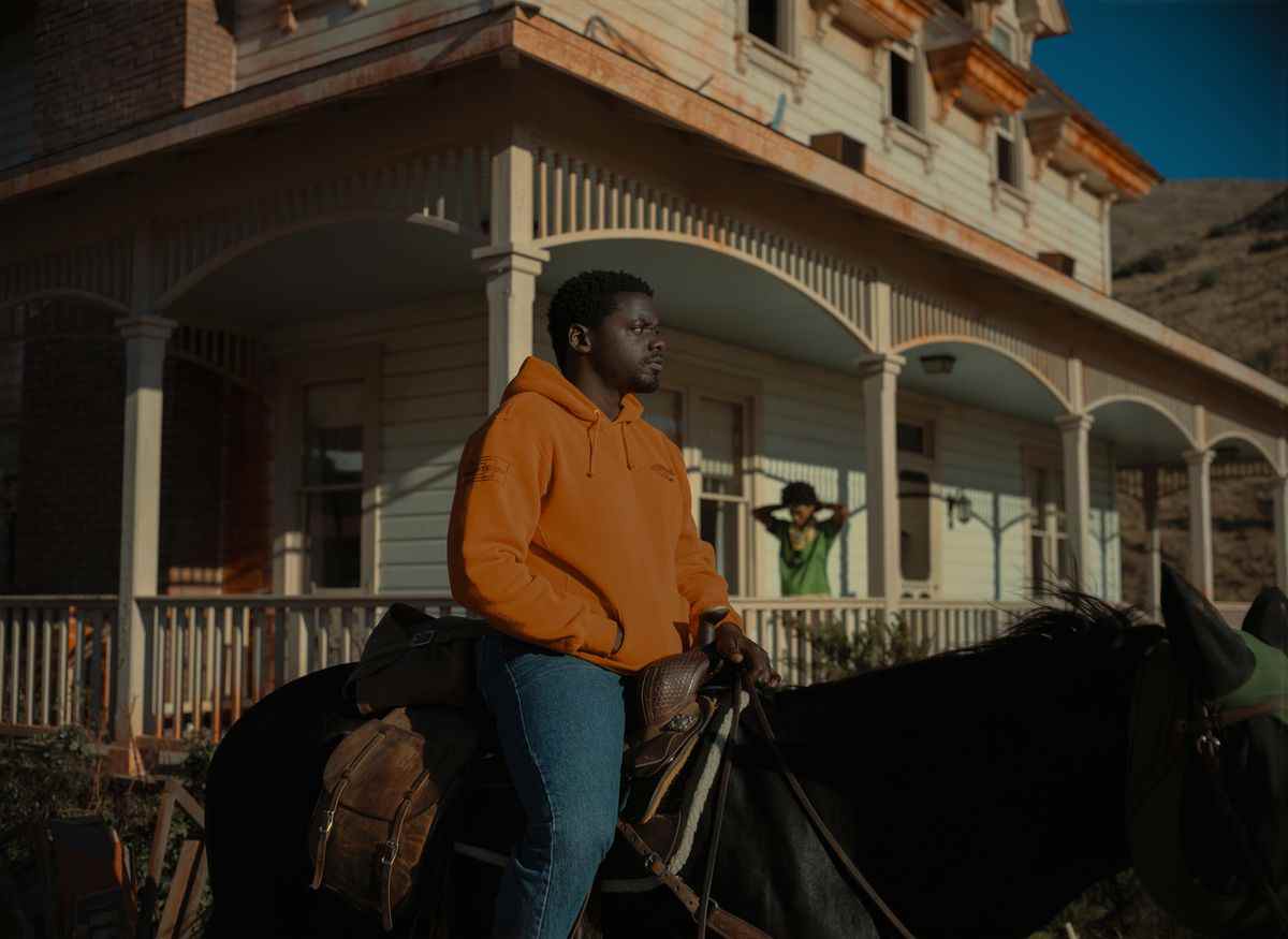 OJ (Daniel Kaluuya), vêtu d'un sweat à capuche orange de marque The Scorpion King, sur un cheval qui se tient devant une maison délabrée, avec sa sœur Emerald (Keke Palmer) debout sur le porche, à Nope