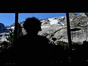 Une personne regarde par la fenêtre du refuge Castiglioni le glacier de Punta Rocca qui s'est effondré près de Canazei, sur la montagne de Marmolada, après qu'une température record de 10 degrés Celsius a été enregistrée au sommet du glacier, le mardi 6 juillet 2022.