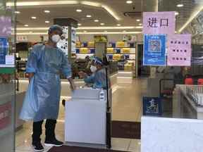 Des travailleurs en tenue de protection surveillent l'entrée d'un magasin, mercredi 6 juillet 2022, à Shanghai.