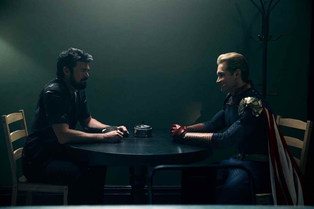Billy et Homelander assis à une table dans une pièce sombre