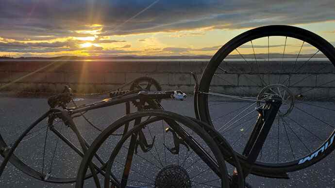 Une photo d'un vélo à l'envers avec la roue arrière éteinte, rétro-éclairé par un coucher de soleil.