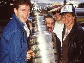 Les Oilers d'Edmonton Kevin Lowe, à gauche, le gestionnaire de l'équipement Lyle 'Sparky' Kulchisky, Mark Messier et Wayne Gretzky détiennent la coupe Stanley après avoir quitté le restaurant David's à Edmonton le 21 mai 1984. Les Oilers ont remporté leur première coupe Stanley le 19 mai 1984.