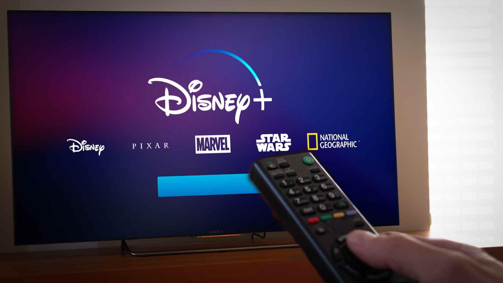 Un homme tenant une télécommande vers un écran affichant le logo Disney Plus