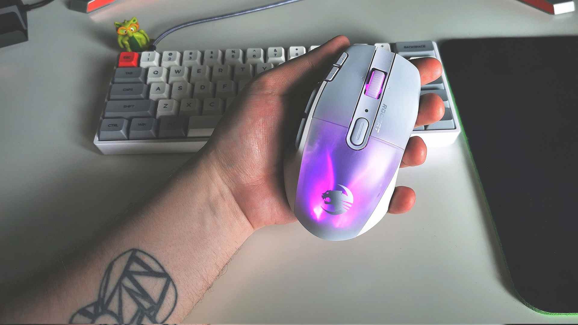 Main tenant la souris de jeu Roccat Kone XP Air à côté d'un clavier blanc