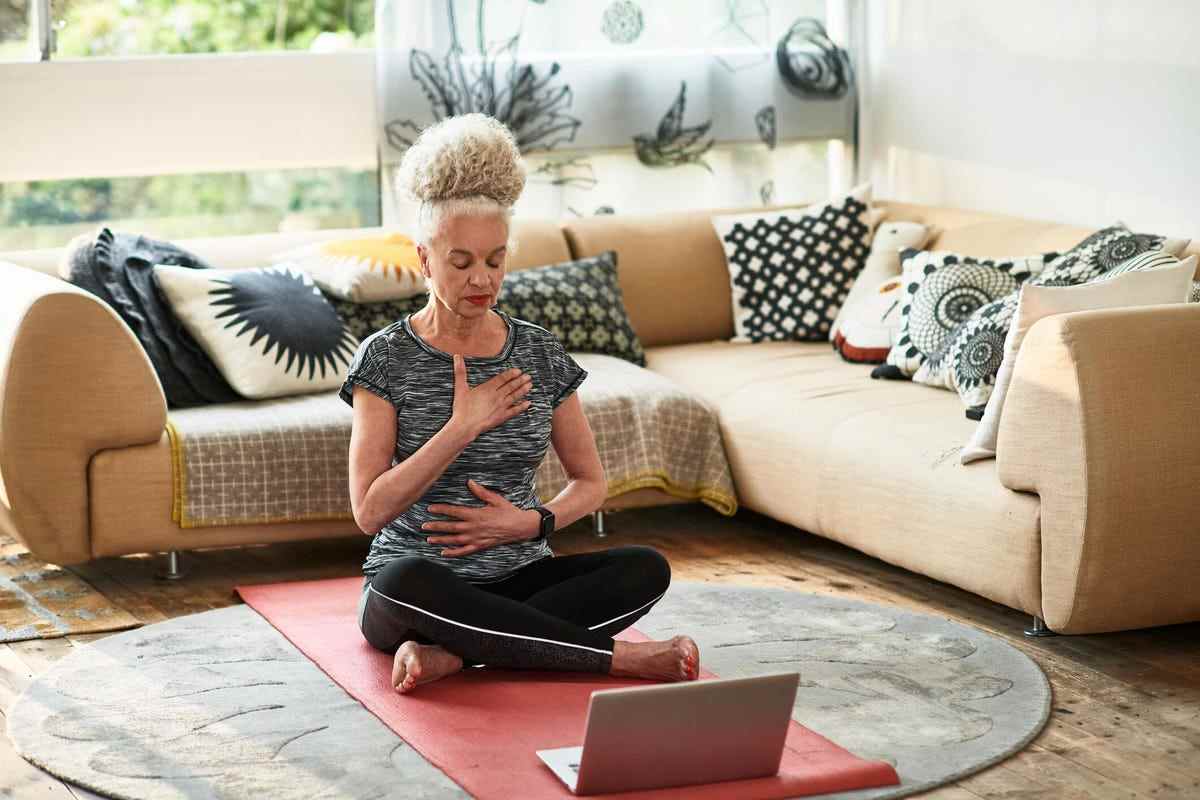 Femme se concentrant sur des exercices de respiration assis sur un tapis de yoga à la maison