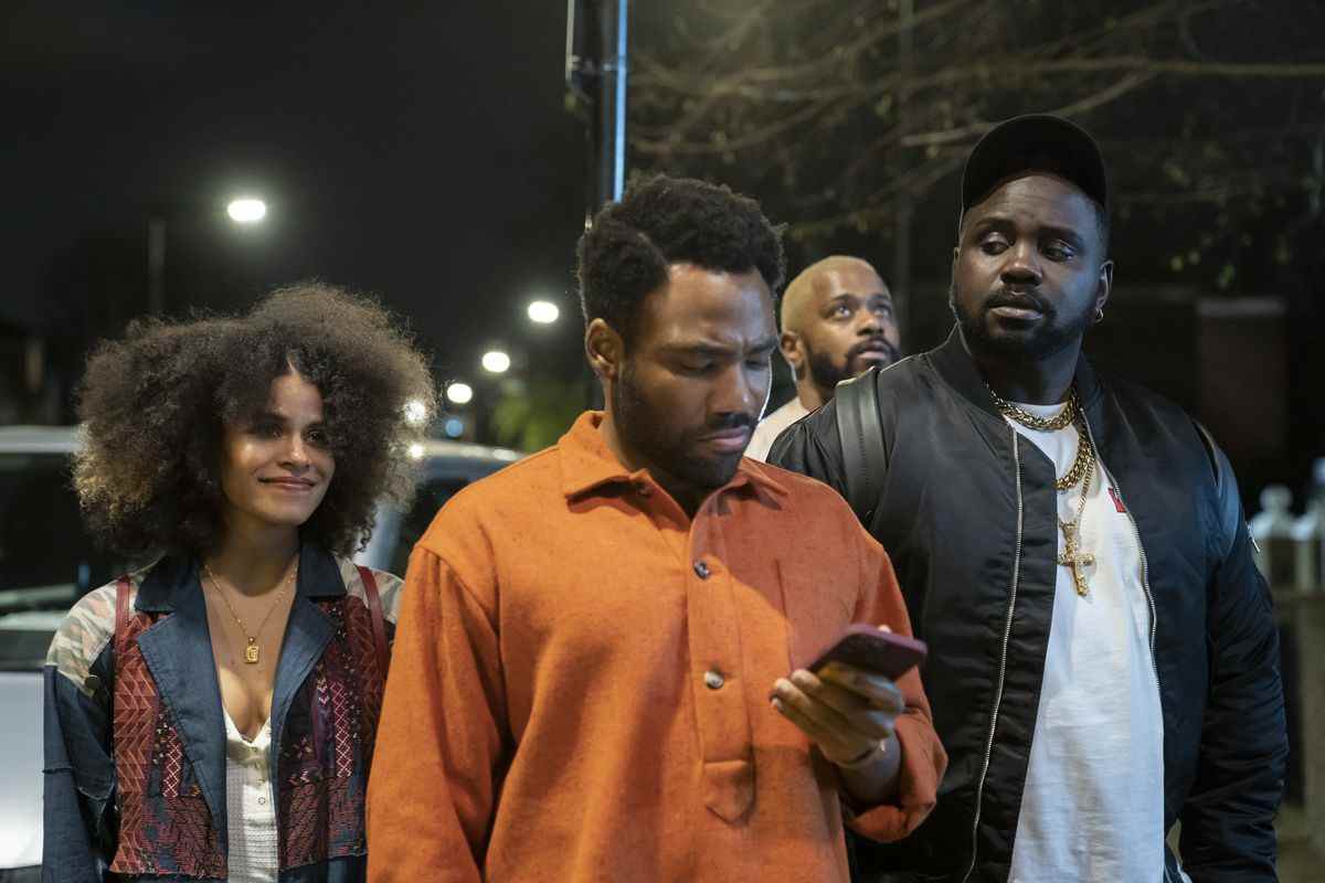 Gagnez en regardant son téléphone tout en marchant dans les rues de la ville la nuit avec Van, Paper Boi et Darius derrière lui dans la saison 3 d'Atlanta