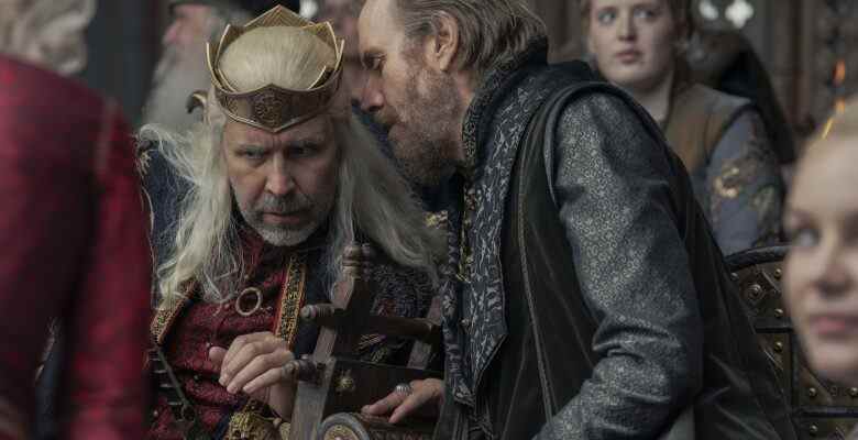 A man with light brown hair whispers in the ear of a medieval king with long white-blond hair; still from "House of the Dragon."