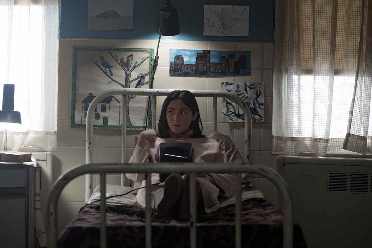 Isabelle Fuhrman comme Esther dans Orphan: First Kill assise sur un lit en lisant un livre