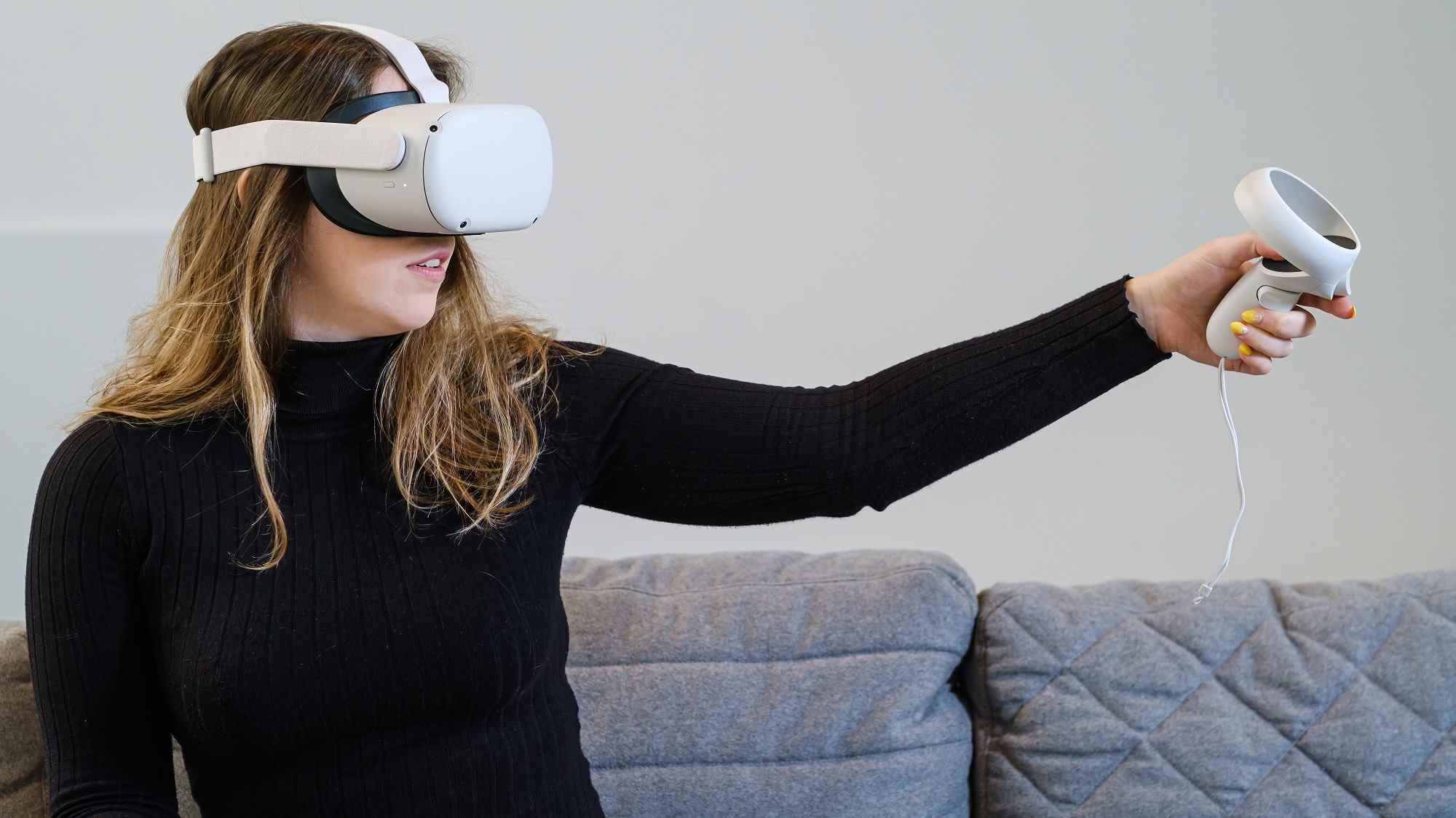 Une jeune femme essaie l'Oculus Quest 2 (Meta Quest 2) pour une expérience virtuelle Assise dans un canapé, vêtue d'un haut noir