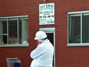 Un enquêteur parle sur un téléphone cellulaire à l'extérieur de l'usine d'Aylmer Meat Packers Inc. le 29 août 2003.