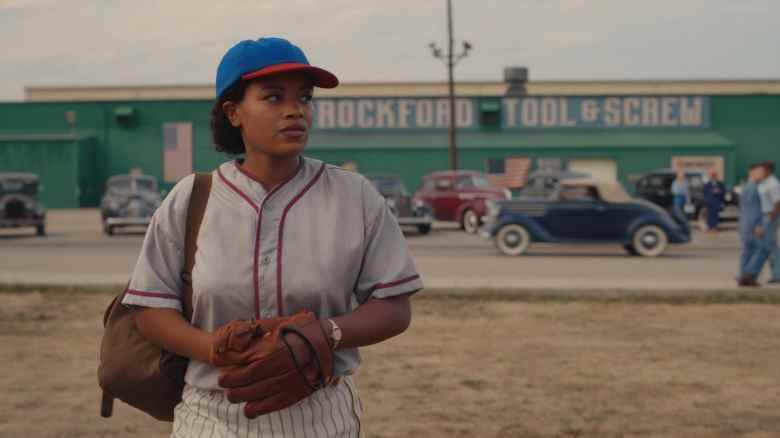 Une femme en uniforme de baseball debout au bord d'un terrain ;  encore de 