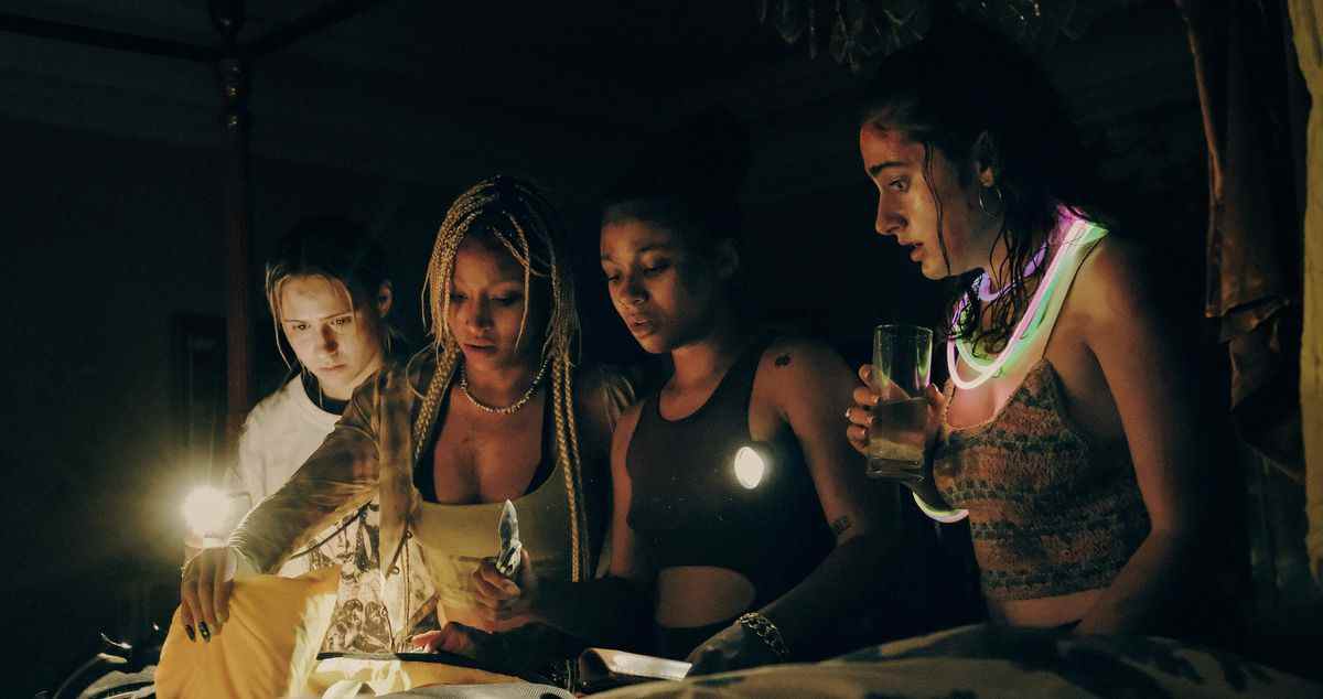 Quatre des femmes de Bodies Bodies Bodies se rassemblent autour d'une bougie dans le noir