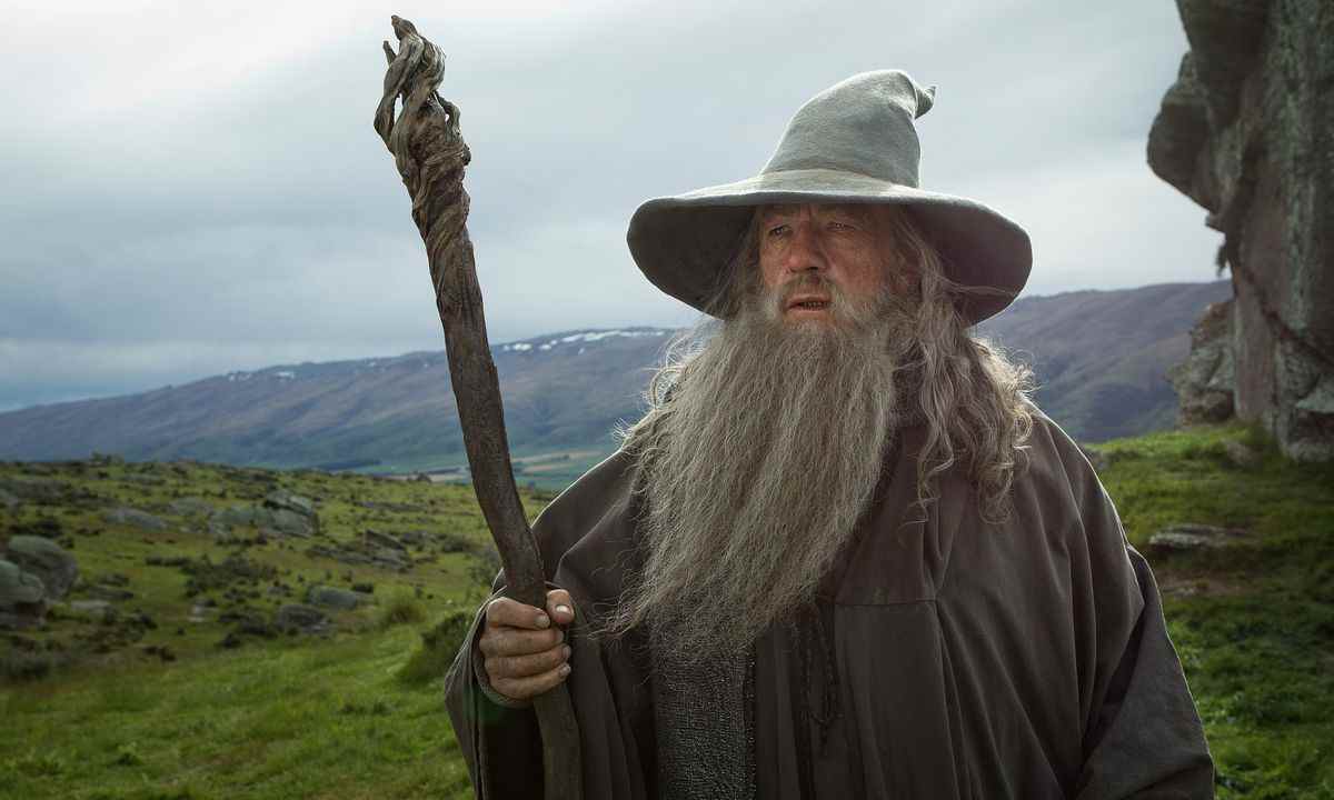 Gandalf le Gris tenant son bâton avec un champ verdoyant et vallonné derrière lui dans Le Hobbit : Un Voyage Inattendu