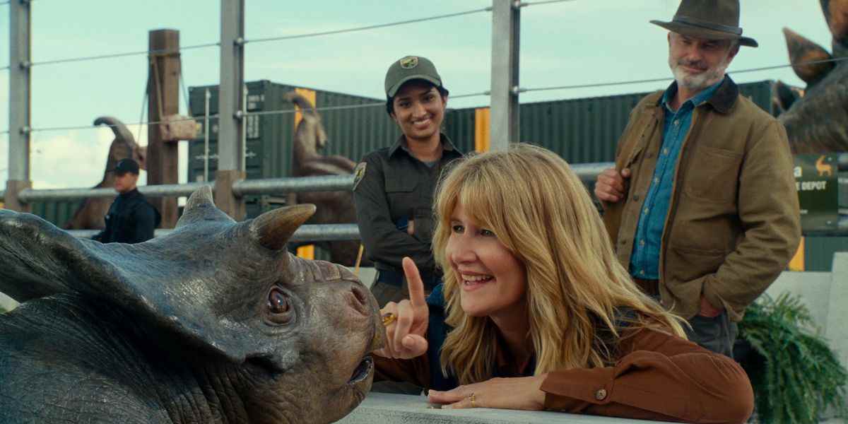 Le Dr Ellie Sattler (Laura Dern) tend un doigt vers un bébé Nasutoceratops d'une manière qui donne l'impression qu'elle est sur le point de le bouffer sur le nez, sous le regard du Dr Alan Grant (Sam Neill) dans Jurassic World Dominion.