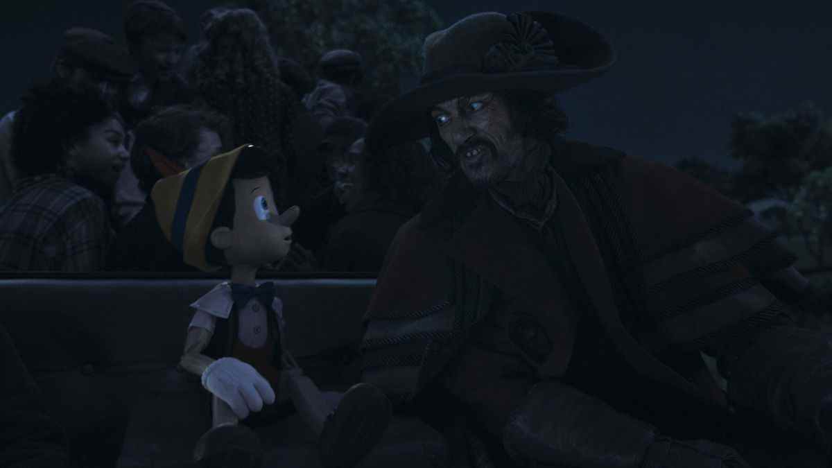 Luke Evans en tant que cocher est assis dans le siège du conducteur de son entraîneur à côté d'un curieux CG Pinocchio dans le remake en direct de Disney de son classique animé de 1940