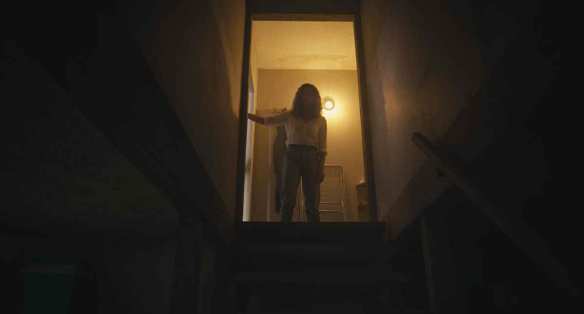 Tess se tient au sommet d'un escalier menant à un sous-sol sombre dans le film d'horreur Barbarian.
