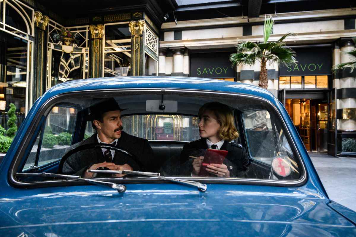 L'inspecteur Stoppard (Sam Rockwell) et l'agent Stalker (Saoirse Ronan) parlent dans une petite voiture de police bleue à l'extérieur de l'hôtel Savoy