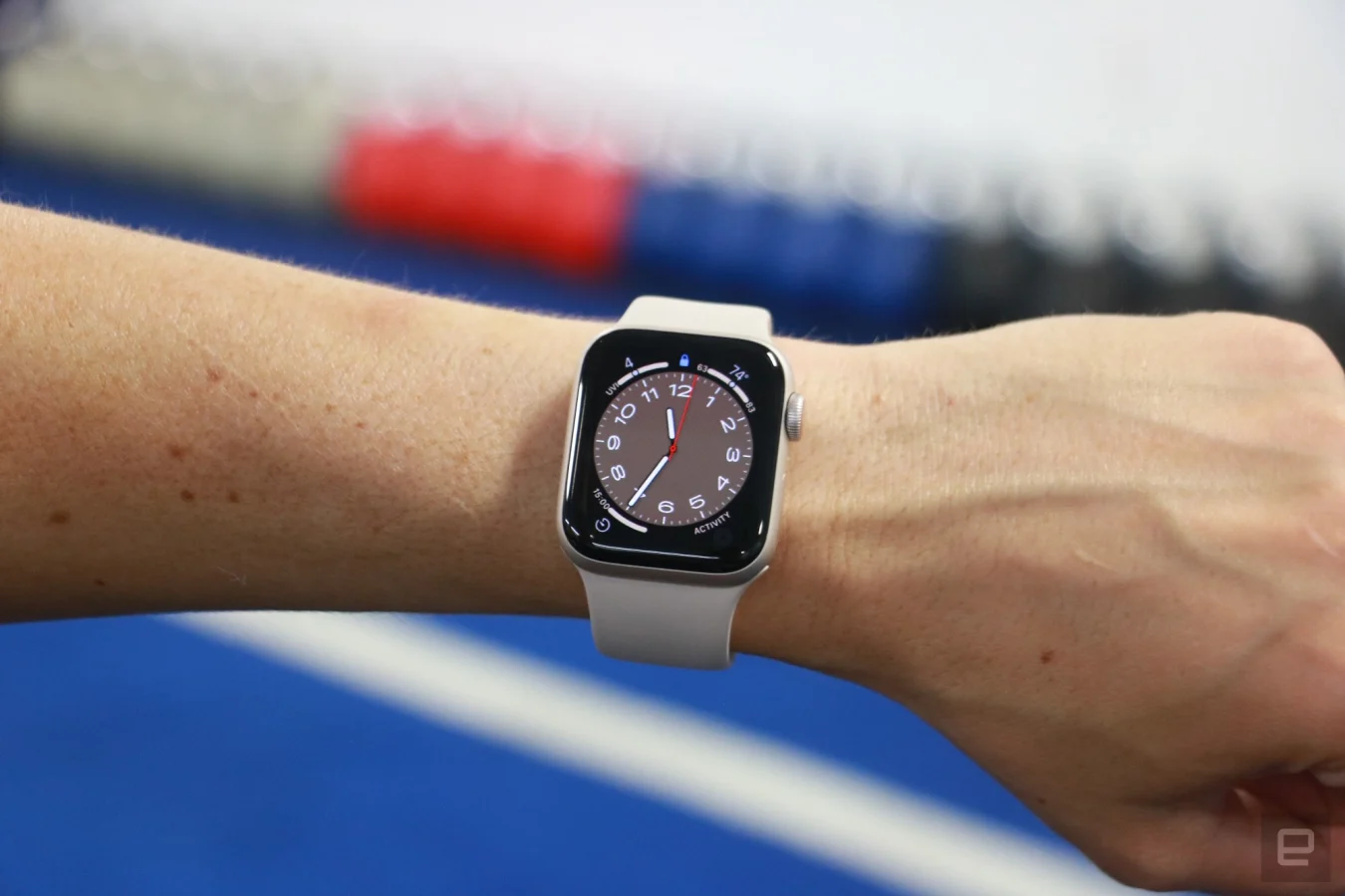 L'Apple Watch SE (2022) au poignet d'une personne tenue devant une rangée colorée de kettlebells.