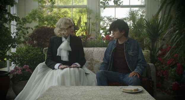 Gwendoline Christie, en tenue fluide noir et blanc, et Asa Butterfield en jean se regardent sur un canapé en Flux Gourmet.