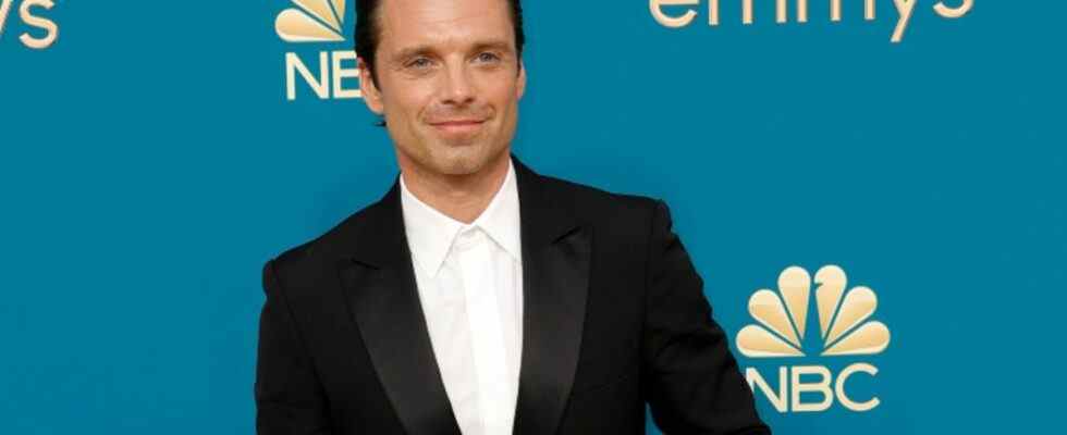 Sebastian Stan walks the carpet at the emmys in a black suit and white button down with no tie.