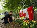 La Canadienne Kersten Samolczyk, qui réside maintenant au Royaume-Uni, place des fleurs près d'un drapeau canadien alors que des milliers de personnes en deuil déposent des fleurs alors que les gens rendent hommage près des portes du palais de Buckingham à Londres le dimanche 11 septembre 2022.