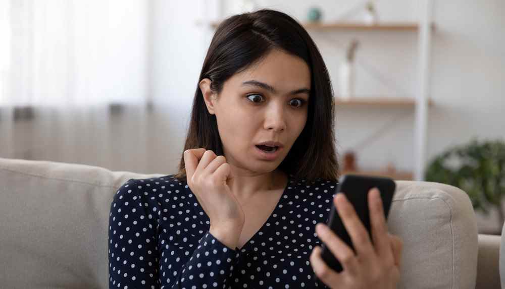 Femme aux cheveux noirs regardant l'écran du smartphone en état de choc.