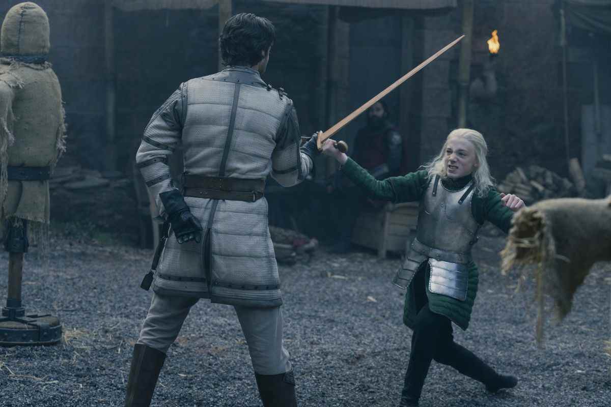Leo Ashton dans le rôle d'Aemond Targaryen, perdant un combat à l'épée.  Il a de longs cheveux brillants et porte une tenue verte recouverte d'une armure de plaques.