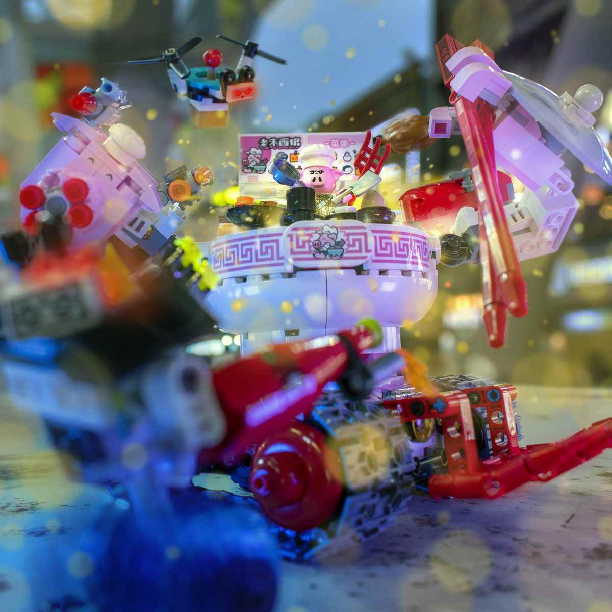 Un chef cochon Lego travaille dans un engin géant à roues construit pour ressembler à un bol de nouilles avec des bras brandissant des baguettes et un acolyte drone.
