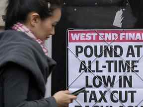 Une femme passe devant un titre affiché sur un mur à Londres.  La Banque d'Angleterre et le gouvernement britannique tentent d'apaiser les marchés inquiets face à la volatilité de l'économie et de la monnaie britanniques.