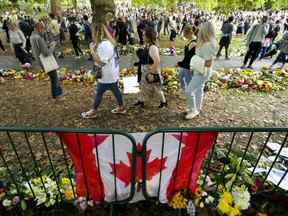 De longues files de personnes en deuil se forment et déposent des fleurs près d'un drapeau canadien alors que les gens attendent de rendre hommage près des portes du palais de Buckingham à Londres le dimanche 11 septembre 2022.