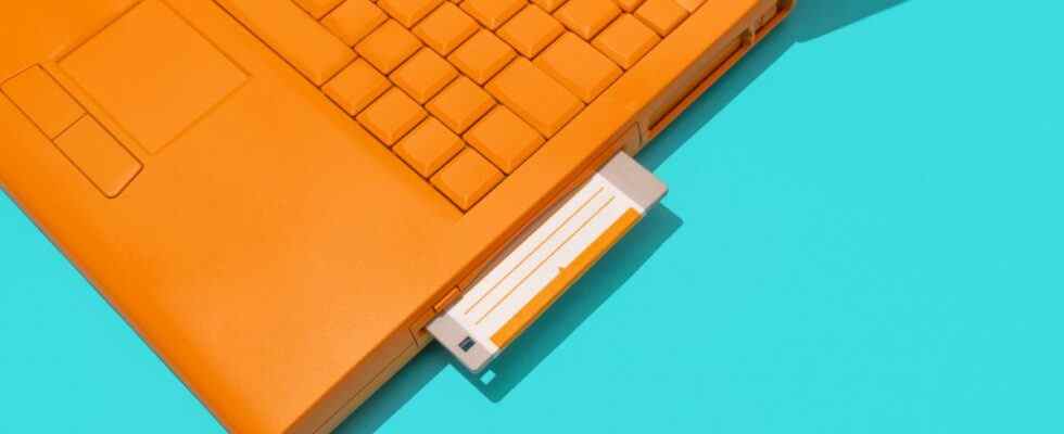 An orange laptop with a floppy disk inserted into it.