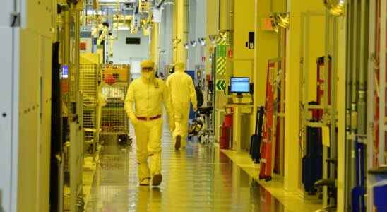 Photograph taken inside an Intel semiconductor fabrication plant showing person in overalls (bunny suit) walking past lithographic equipment.