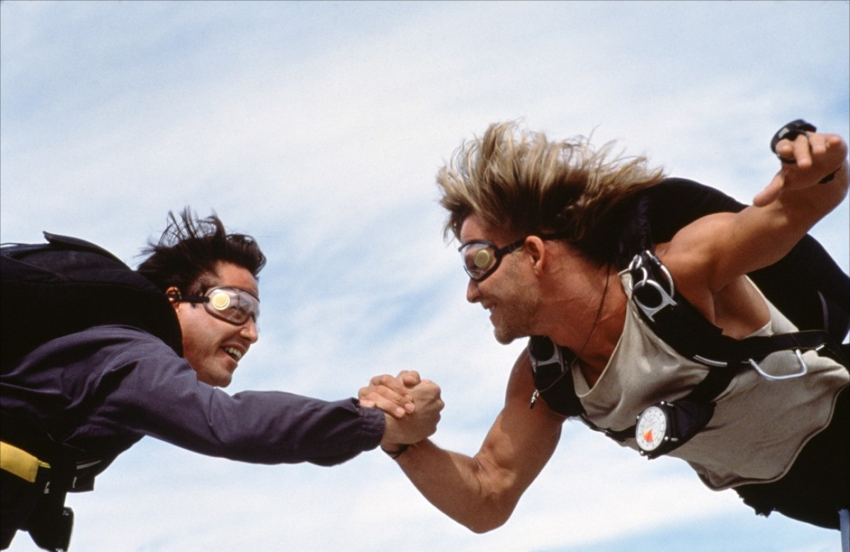 Patrick Swayze et Keanu Reeves se serrent la main et se regardent dans les yeux en faisant du parachutisme dans Point Break.