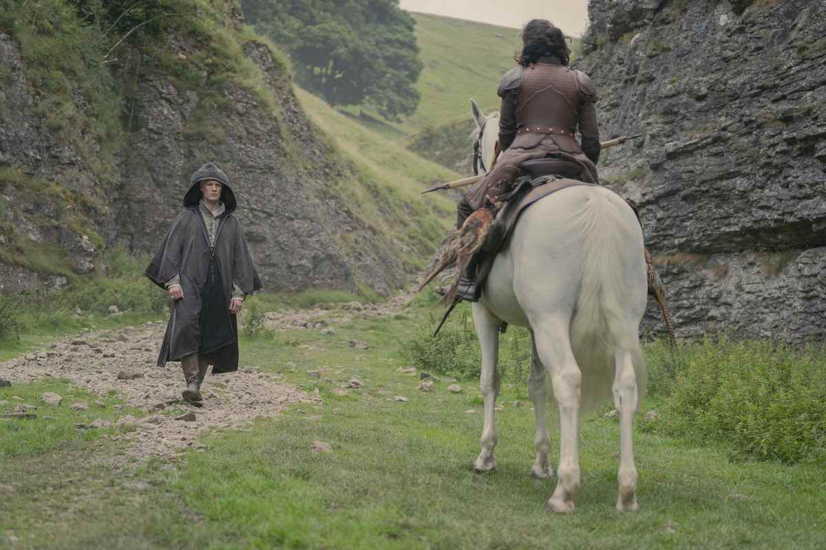 Démon debout avec une cape et sa capuche relevée, marchant vers une femme à cheval nous tournant le dos