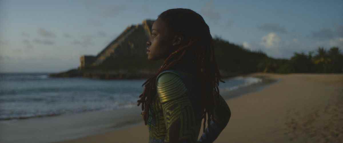 Lupita Nyong'O dans le rôle de Nakia, debout sur une plage face à l'océan dans Black Panther : Wakanda Forever. 