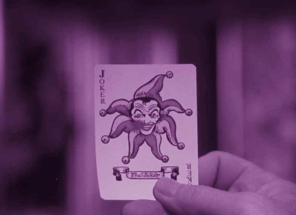 Un alambic teinté de violet d'un homme tenant une carte à jouer Joker dans Batman: The Silent Motion Picture.