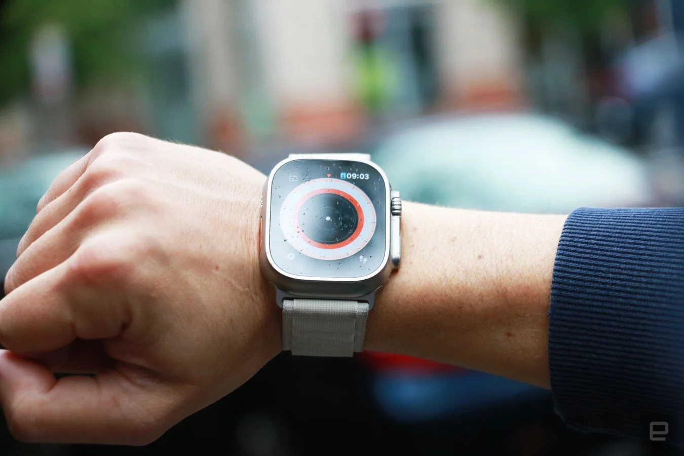 L'Apple Watch Ultra avec bracelet à boucle alpine au poignet d'une personne.  L'écran affiche la soi-disant vue technique de l'application Compass, avec un point blanc au milieu. 